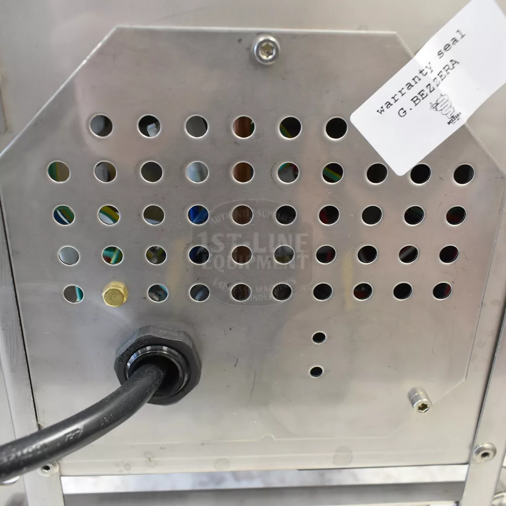 A close-up of the Bezzera Matrix MN V2 Dual Boiler Espresso Machines metal panel shows multiple circular holes, a thick black cable at the bottom left, and a Warranty Seal G. BEZERRA sticker in the upper right corner. © 2025 1st-line.com