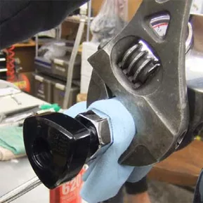 A close-up of a wrench tightening a plumbing valve wrapped in a blue cloth, with tools and supplies visible in the background—ideal for steam valve gasket repair. © 2025 1st-line.com