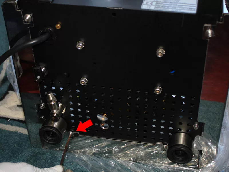 A gloved hand uses a tool on the underside of a machine with two wheels; a red arrow points to an area near the left wheel, highlighting a specific spot for Water Tank Repair. © 2025 1st-line.com