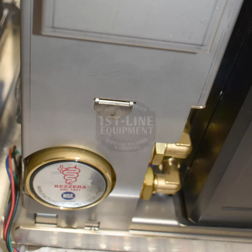 Close-up of a Bezzera Matrix MN V2 Dual Boiler Espresso Machine’s internals, showing the round Bezzera pressure gauge, brass fittings, wires, metallic housing, and a subtle 1st-Line Equipment logo. © 2025 1st-line.com