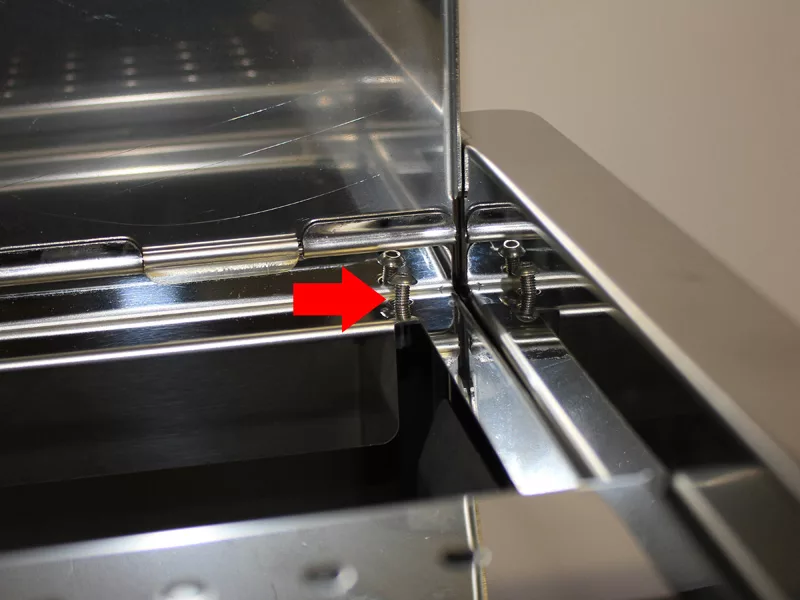 Close-up of a shiny metal surface with a red arrow pointing to two small screws in the corner, indicating the location for Water Tank Repair or adjustment of the water tank manifold during assembly. © 2025 1st-line.com