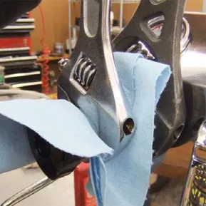Close-up of a wrench gripping a bike part, with a blue cloth protecting the surface—similar care used in steam valve gasket repair. Shelves with tools are visible in the blurry background. © 2025 1st-line.com