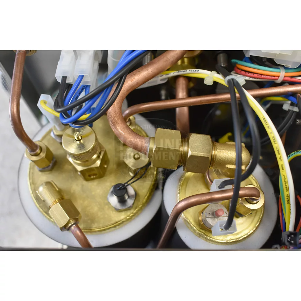 Close-up of brass and copper pipes, fittings, wires, and connectors inside the Bezzera Matrix MN V2 Dual Boiler Espresso Machine, highlighting its detailed electrical and plumbing components. © 2025 1st-line.com
