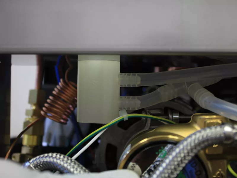 Close-up view of components inside a machine, showing plastic tubes, a coiled copper pipe, wires, and metal parts—likely part of a coffee machine’s internal mechanism related to water tank repair. © 2025 1st-line.com