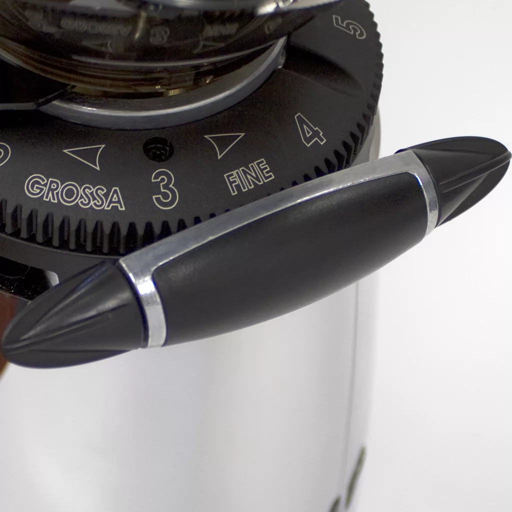 Close-up of the discontinued Macap M42 Stepless Doser Espresso Coffee Grinder’s grind size selector with a black handle, numbered dial (3–5), marked GROSSA (coarse) and FINE. A stepless doser and metallic-black finish add sleek style. © 2025 1st-line.com