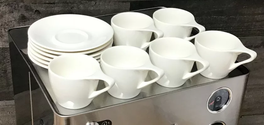 Six white ceramic cups and saucers are stacked on top of the Lelit Elizabeth V3 Dual Boiler Espresso Machine, a sleek model featuring control knobs and a front-facing gauge. © 2025 1st-line.com