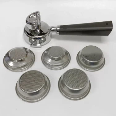 The Lelit PLA582W Dual Spout Wood Handle Portafilter Kit is shown with five metal filter baskets, each featuring a unique perforated or mesh design, displayed on a white background. © 2025 1st-line.com