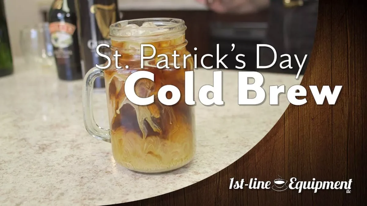 A glass mug of iced cold brew coffee with cream swirls sits on a counter. Text reads “St. Patrick’s Day Cold Brew.” The 1st-line Equipment logo appears at the bottom right. Bottles are blurred in the background. © 2025 1st-line.com