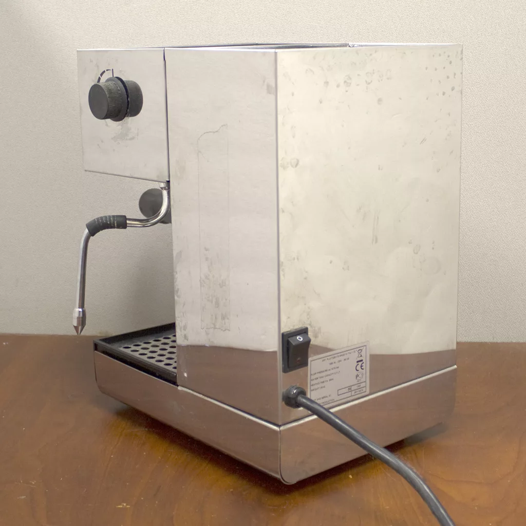 A used Lelit PL41TQE Anna Espresso Machine with stainless steel body, steam wand, black knob, and power cord is placed on a wooden surface against a light wall. © 2025 1st-line.com