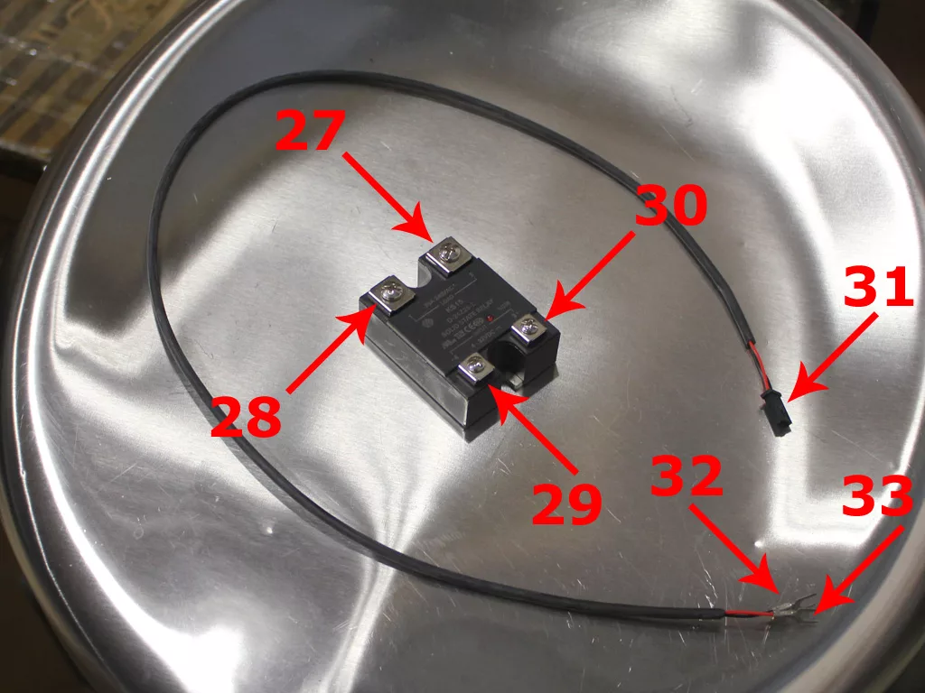 A black electronic relay with four screw terminals, used in VBM Dual Boiler 3.5 to 4.0 conversion, is placed on a metallic tray. Two wires extend from the relay, highlighted by red numbers (27–33) indicating key components. © 2025 1st-line.com