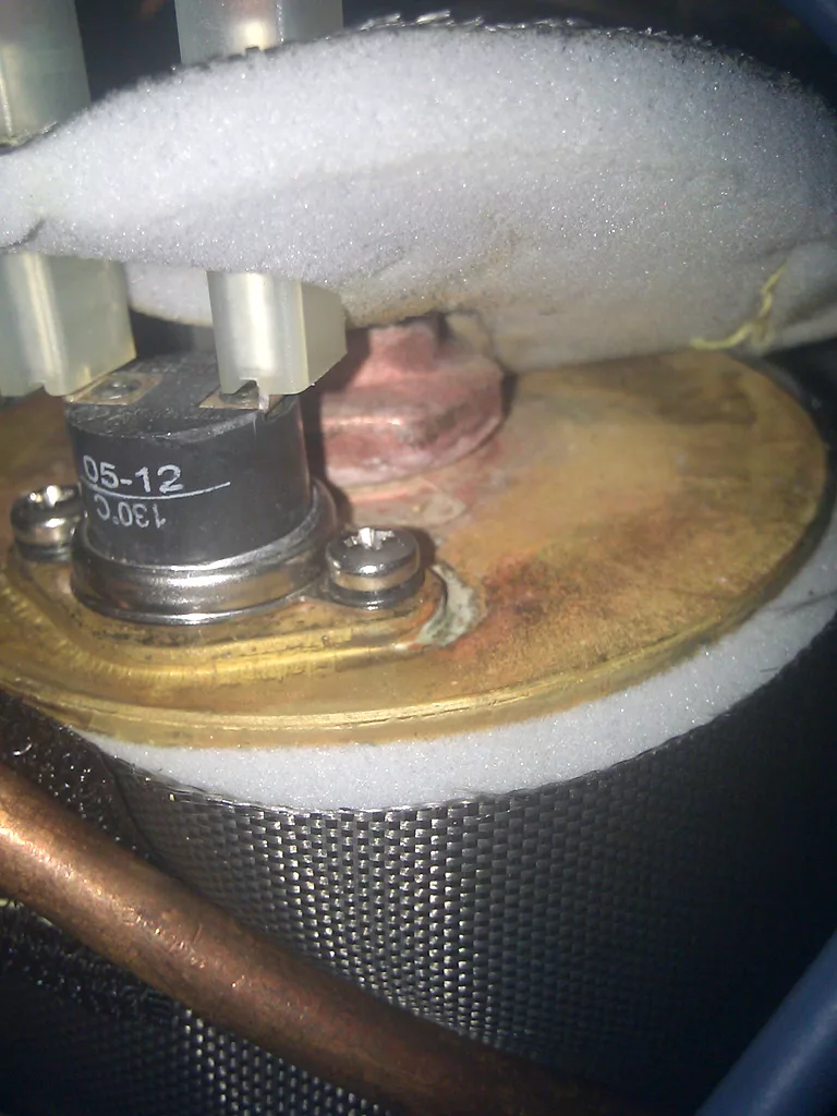 Close-up of a frosted metal component inside a mechanical or refrigeration unit, showing ice buildup and possible limescale on pipes and fittings, with visible screws, wiring, and copper tubing that may indicate leakage issues. © 2025 1st-line.com