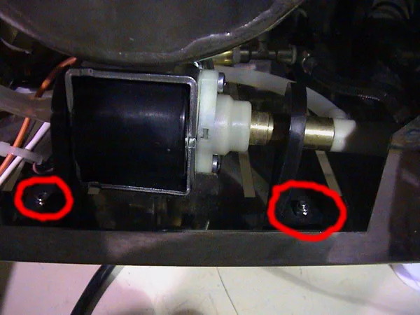 Close-up of a mechanical component, possibly for pump repair, featuring a black cylindrical part and two screws circled in red on a metal base. Some wires and tubes are visible on the left side. © 2025 1st-line.com