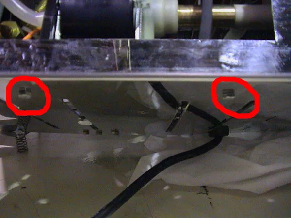 Close-up of a metallic surface with two screws circled in red, black wires running across the bottom, and reflection of machine parts at the top—typical details seen during valve repair or pump repair procedures. © 2025 1st-line.com