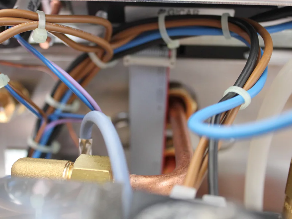 Close-up of electrical wires and copper pipes secured with zip ties inside a device, highlighting various colored cables, components, and a PID display for monitoring performance. © 2025 1st-line.com