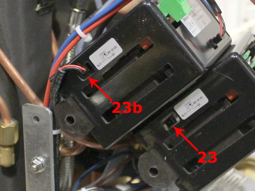 Close-up of two black electrical components with labels and wires attached; red arrows labeled 23 and 23b point to each component inside a VBM Dual Boiler, possibly related to a 3.5 to 4.0 conversion process. © 2025 1st-line.com