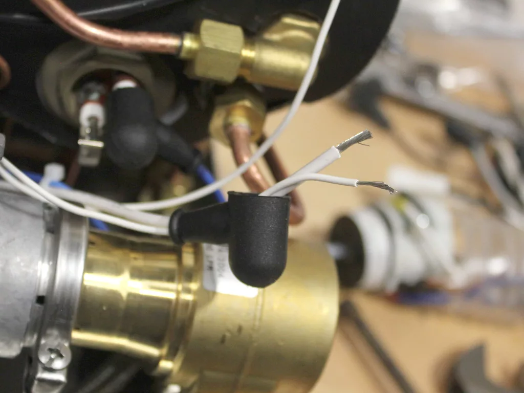 Close-up of two exposed white wires beside brass and copper components, likely part of a VBM Dual Boiler machine being repaired or 3.5 to 4.0 conversion, with tools visible in the blurry background. © 2025 1st-line.com