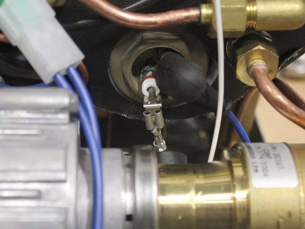 Close-up view of an electronic component with wires and connectors attached, surrounded by copper pipes and metallic parts—possibly showcasing a VBM Dual Boiler upgrade from 3.5 to 4.0 in industrial equipment. © 2025 1st-line.com