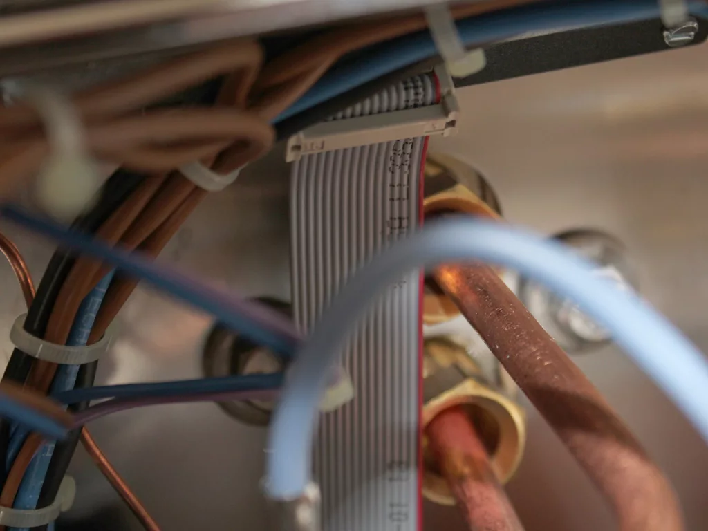 Close-up view of electrical wires and cables, including a flat ribbon cable and copper pipes, secured with zip ties inside an electronic device—potential sources to check for PID Display Issues. © 2025 1st-line.com
