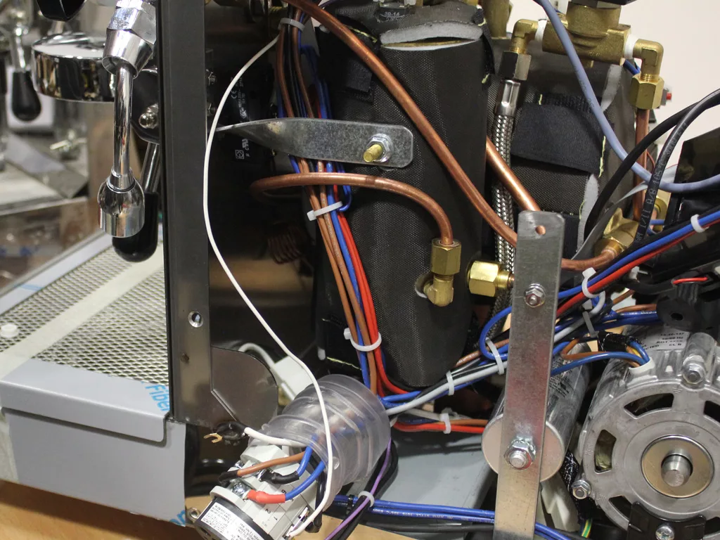 Close-up view of the inside of a VBM Dual Boiler coffee machine, showing various wires, tubes, copper pipes, a pump, and an electric motor. Some parts are labeled or mounted to a metal frame for 3.5 to 4.0 conversion. © 2025 1st-line.com