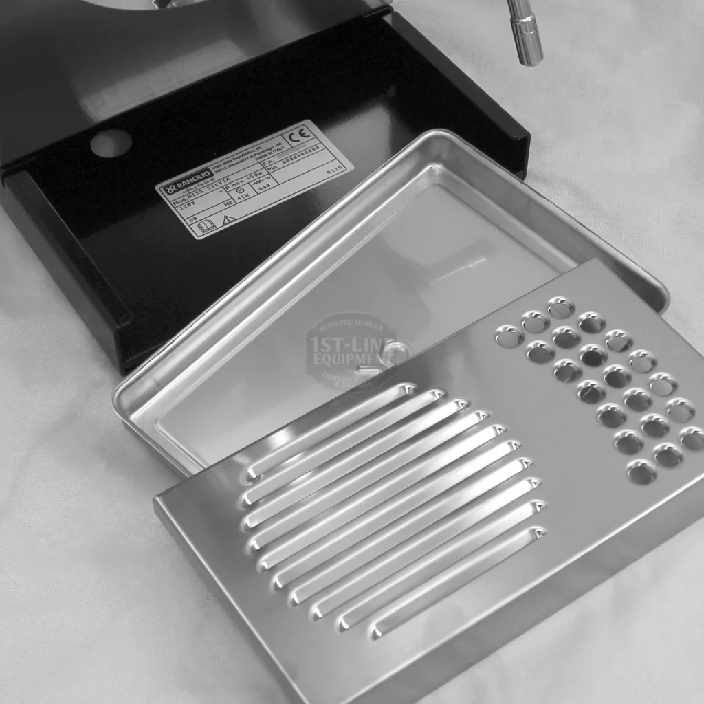 A close-up of a disassembled Rancilio Silvia espresso machine drip tray set on a counter, showing both the slotted grate and the perforated tray beside the machine base for accessing inside. © 2025 1st-line.com