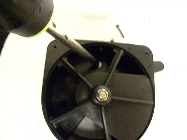 A screwdriver is being used to unscrew a screw from a black plastic fan or vent cover, with one screw already removed and lying nearby—possibly as part of Rancilio Support or technical maintenance. © 2025 1st-line.com