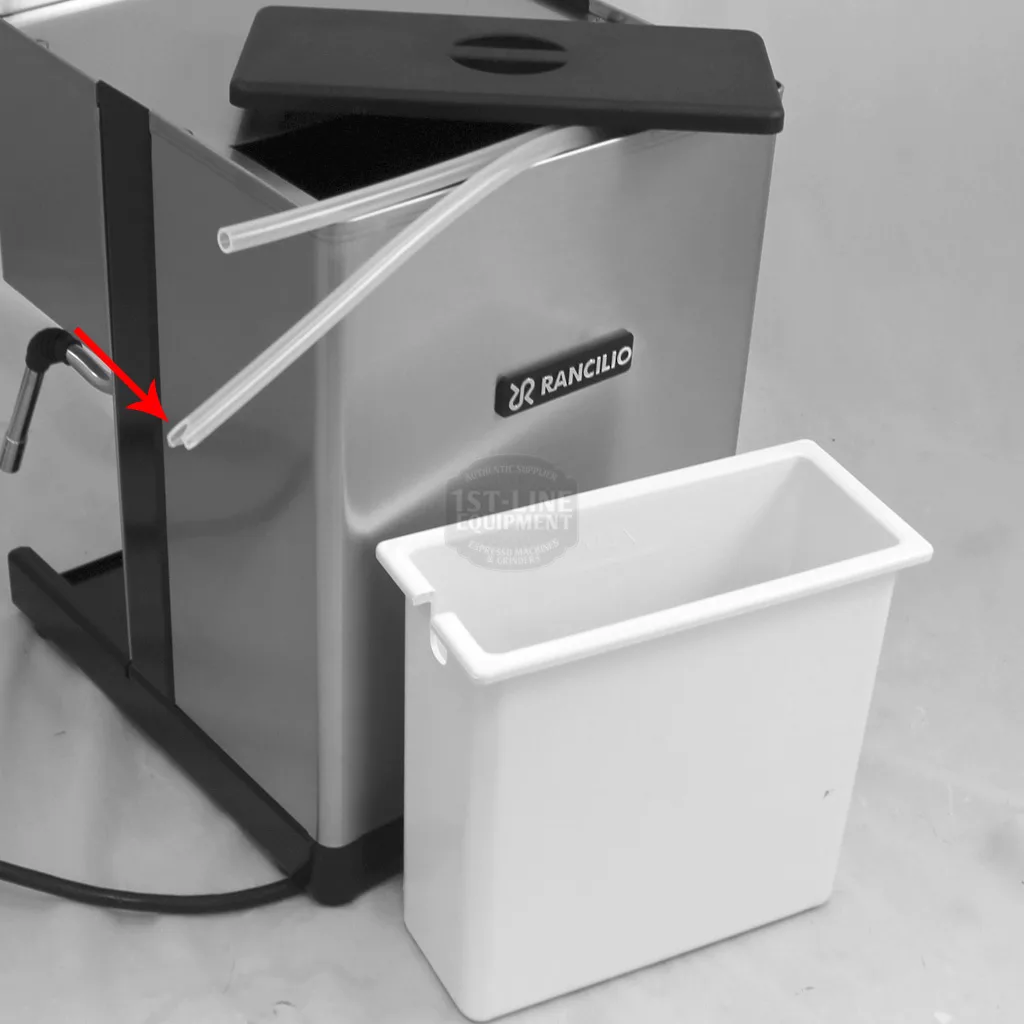 A stainless steel Rancilio Silvia coffee machine with a black lid, two clear tubes extending from the side, and a white rectangular plastic container placed in front. A red arrow points to one of the tubes for accessing inside. © 2025 1st-line.com