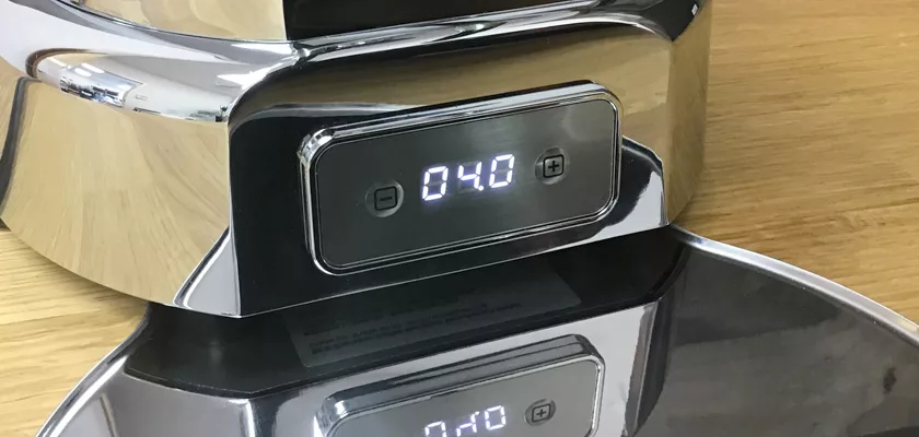 A close-up of a DISCONTINUED ECM V-Titan 64 Espresso Grinder with a metallic finish, screen displaying 040, on a wooden surface, with its display and part of the grinder reflected on the shiny surface below. © 2025 1st-line.com
