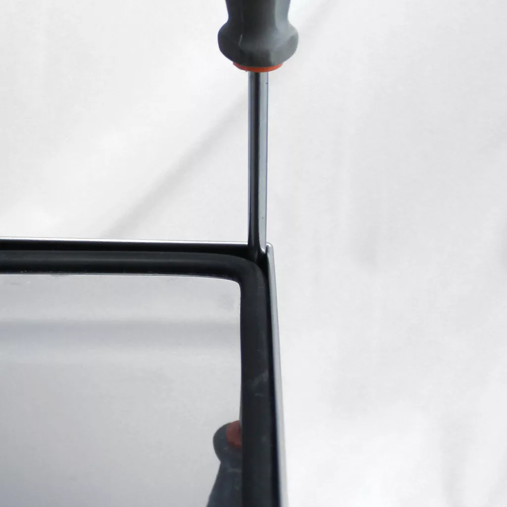 A close-up of a screwdriver being used to pry open the corner of a black electronic device, possibly an espresso machine like the Lelit Anna, against a plain white background. © 2025 1st-line.com