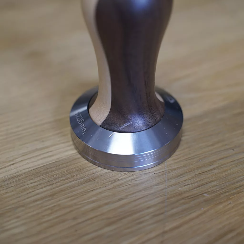 A metal espresso tamper with a wooden handle rests on light wood, perfect for use with the (SOLD) SIDEWALK SALE - Lelit PL41TEM Anna Espresso Machine (returned & refurbished). The base is engraved 52.5 mm. © 2025 1st-line.com