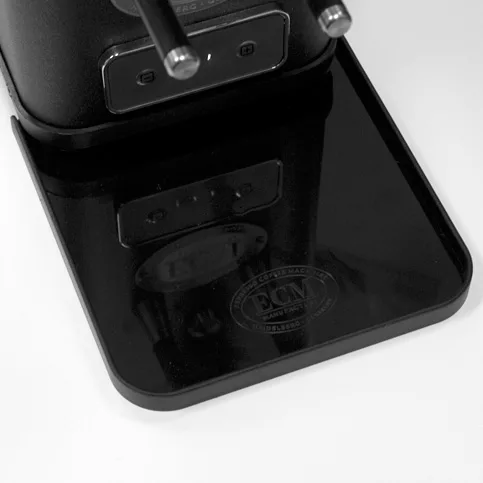 Close-up of a polished black drip tray on an espresso machine, reflecting part of the ECM S-Automatik 64 Espresso Grinder above. The trays surface features an impressively etched or printed ECM logo. © 2025 1st-line.com