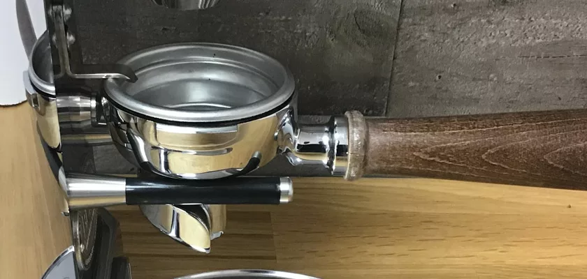 Close-up of a portafilter with a wooden handle on an espresso machine above a drip tray—perfectly matched with the discontinued ECM V-Titan 64 Espresso Grinder. © 2025 1st-line.com
