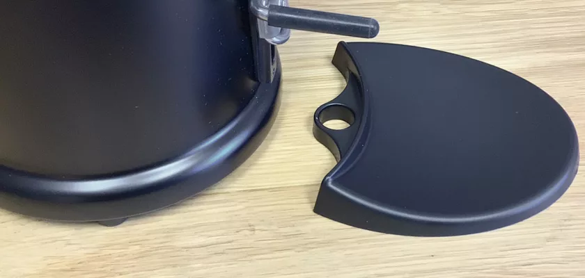 A black plastic drip tray is shown detached and lying beside the base of an Elektra MSD Espresso Coffee Grinder on a wooden surface. © 2025 1st-line.com