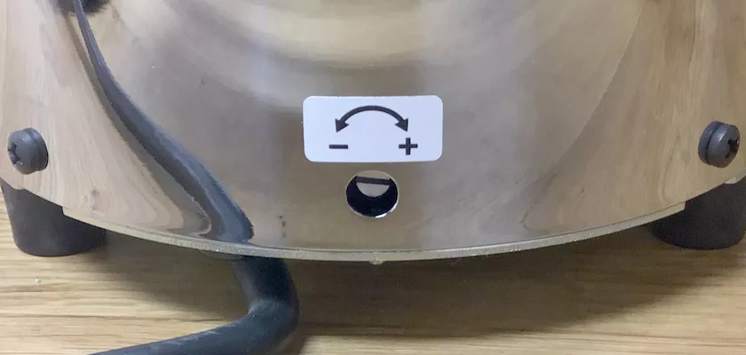 A close-up of the DISCONTINUED 1st-line Sonny Espresso Coffee Grinder with a black cord, showing an adjustable settings label above a small hole, sits on a wooden surface. © 2025 1st-line.com