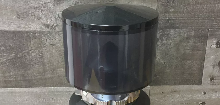 A glossy, black cylindrical DISCONTINUED 1st-line Sonny Espresso Coffee Grinder with a domed top rests on a textured gray wood-patterned surface and background. © 2025 1st-line.com