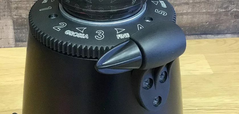 Close-up of the Elektra MSD Espresso Coffee Grinder’s black dial labeled “GROSSA” and “FINE,” featuring a prominent lever and screws, set on a wooden surface with a blurred background. © 2025 1st-line.com