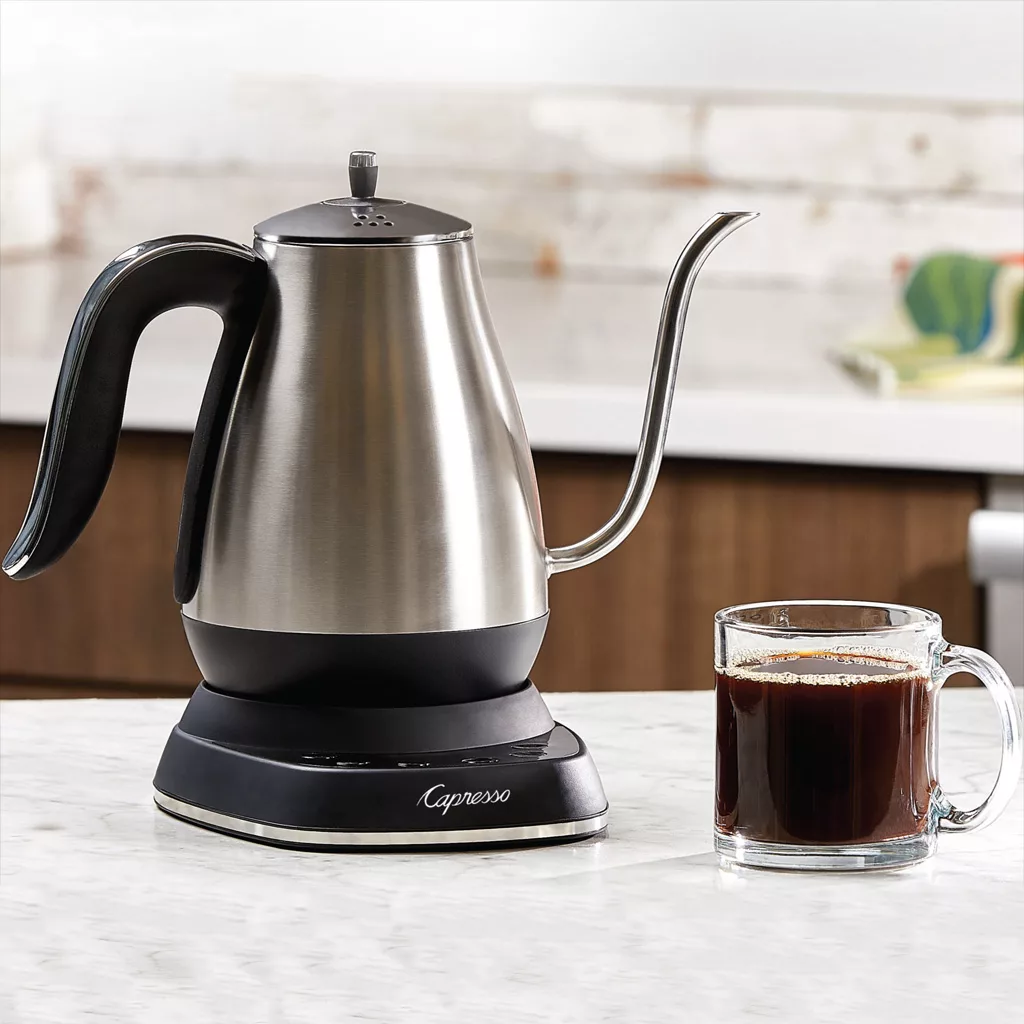 A Capresso 290.05 Electric Pour Over Water Kettle sits on a modern kitchen countertop next to a clear glass mug of black coffee, highlighting this sleek kettle’s style and precision. © 2025 1st-line.com