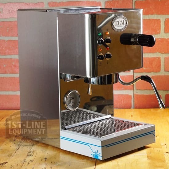 A RETURNED & REFURBISHED - ECM Casa V Espresso Machine (C102) with steam wand, pressure gauge, and control buttons sits on a wooden countertop in front of a red brick wall. © 2025 1st-line.com
