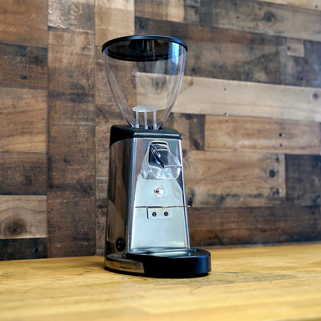 A SIDEWALK SALE - Ascaso I-2 Doserless Conical Burr Stepless Espresso Coffee Grinder E209 with a clear plastic hopper sits on a wooden countertop in front of a rustic wood panel wall. © 2025 1st-line.com