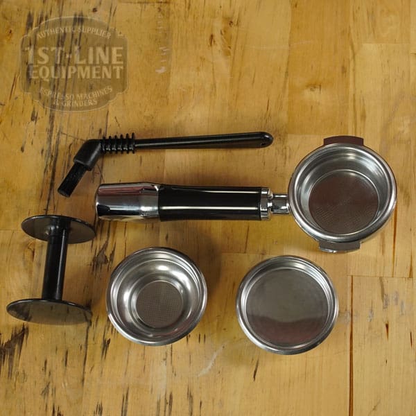 Accessories from the RETURNED & REFURBISHED - ECM Casa V Espresso Machine (C102)—including a portafilter, tamper, cleaning brush, and three filter baskets—are neatly arranged on a wooden surface. © 2025 1st-line.com