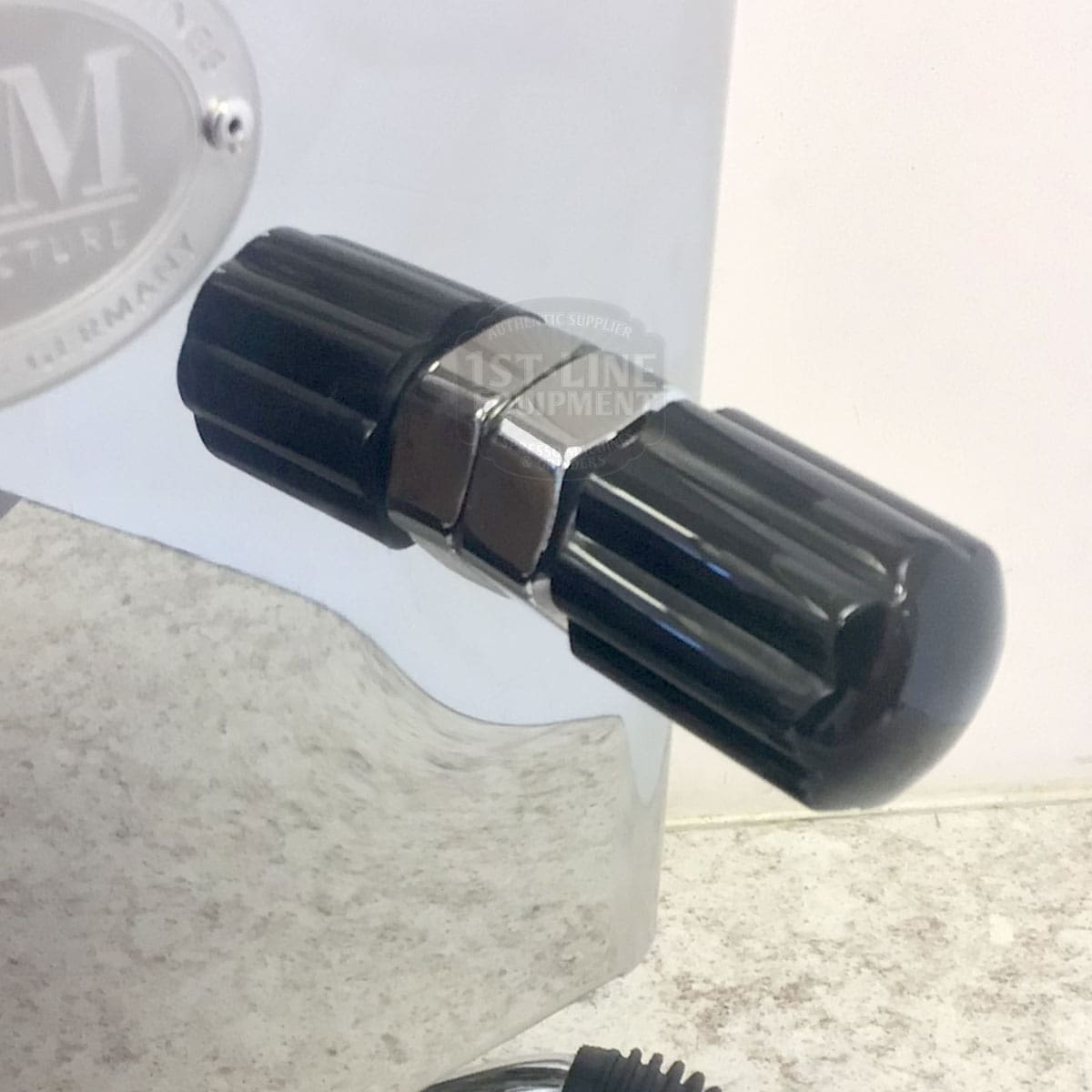 Close-up of a black, ridged knob on the shiny metallic surface of a RETURNED & REFURBISHED - ECM Casa V Espresso Machine (C102), shown above a textured countertop. © 2025 1st-line.com