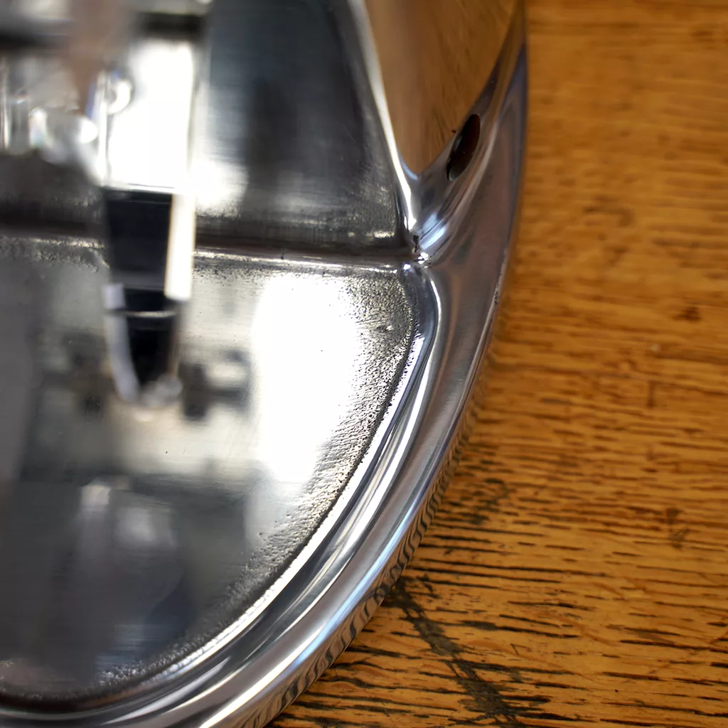 Close-up of a shiny metal base of an iron on wood, its reflections echoing the polished finish of the Ascaso I-2 Doserless Conical Burr Stepless Espresso Coffee Grinder E209 from our SIDEWALK SALE. © 2025 1st-line.com