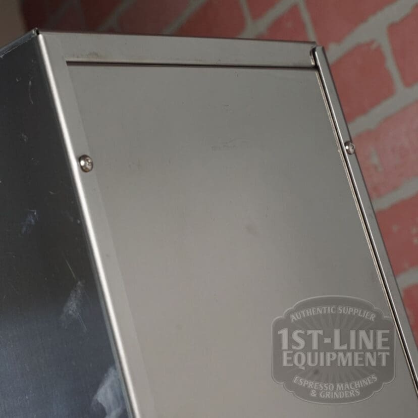 A close-up of a RETURNED & REFURBISHED - ECM Casa V Espresso Machine (C102) shows its stainless steel design and visible screws, with a red brick wall backdrop. The 1st-Line Equipment Espresso Machines & Grinders logo is in the bottom right. © 2025 1st-line.com