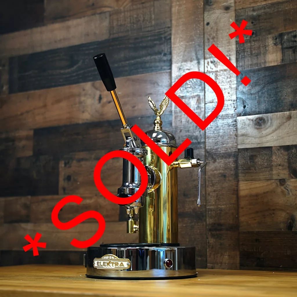 A (SOLD) SIDEWALK SALE - Elektra S1CO Microcasa A Leva Espresso Machine - Chrome & Brass (Returned and Refurbished) is displayed on a wooden surface with a dark wood wall behind and large red “*SOLD!*” text across the image. © 2025 1st-line.com
