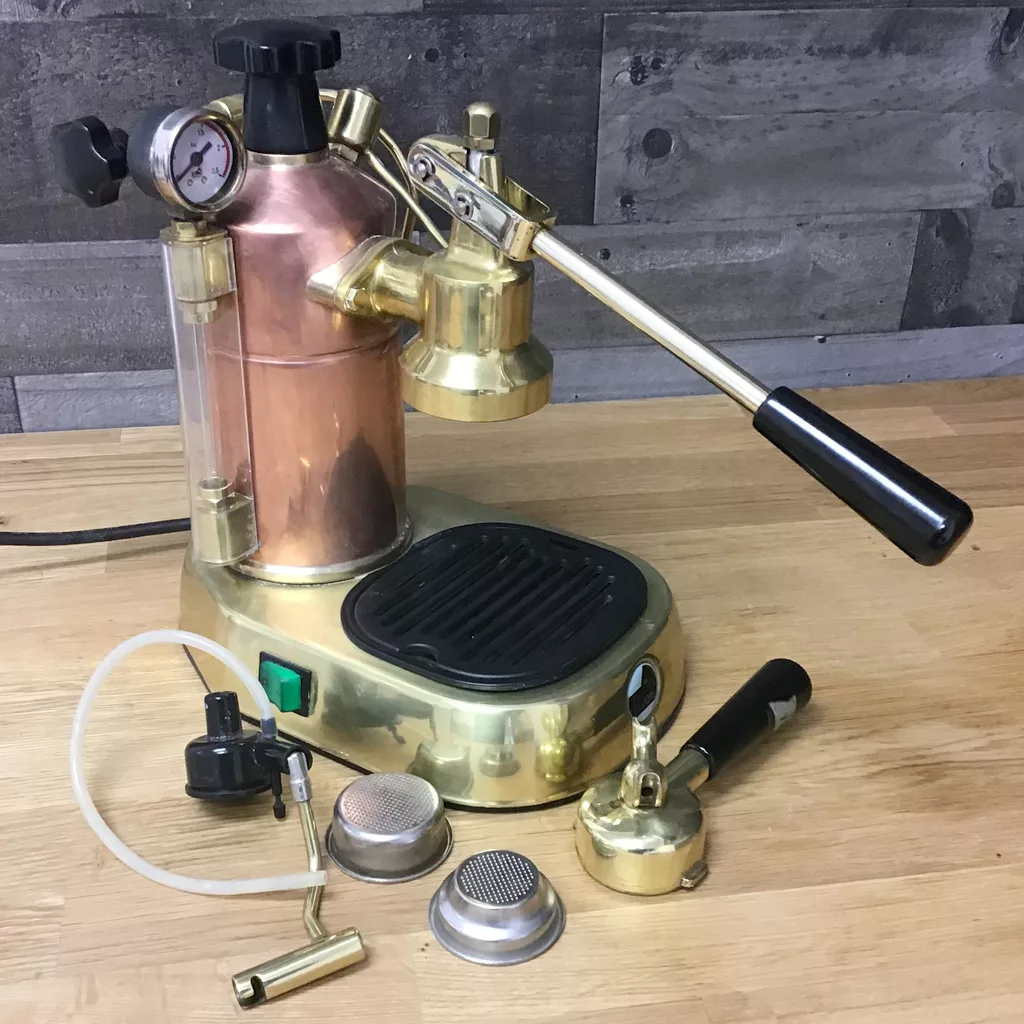 A (SOLD) SIDEWALK SALE - PRE-MILLENIUM La Pavoni Professional Copper & Brass Espresso Machine (16 cup, USED) with lever and pressure gauge sits on a wooden counter, with accessories like portafilter, baskets, and tubing in front. © 2025 1st-line.com