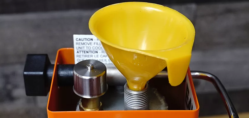 A yellow funnel is inserted into a metal container, with a caution label and orange frame surrounding a DISCONTINUED Ponte Vecchio Export Spring Piston Lever Espresso Machine. © 2025 1st-line.com
