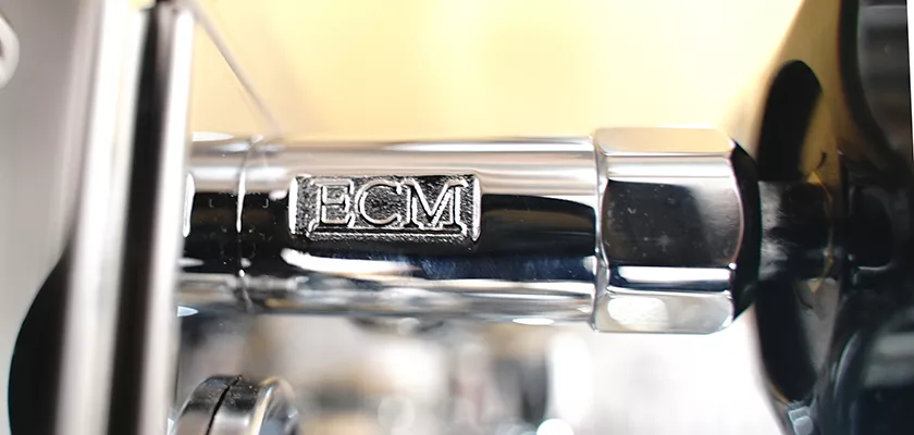 Close-up of a shiny metal part from the DISCONTINUED ECM Mechanika V Slim Espresso Machine with “ECM” engraved, reflecting light and displaying premium craftsmanship in its polished finish. © 2025 1st-line.com