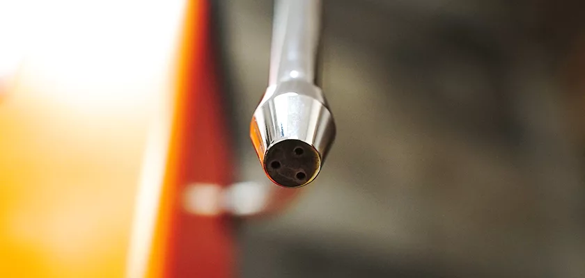 Close-up of a silver dental tool, echoing the precision of a DISCONTINUED Ponte Vecchio Export Spring Piston Lever Espresso Machine, featuring three small holes at its tip against a blurred orange-tinged background. © 2025 1st-line.com
