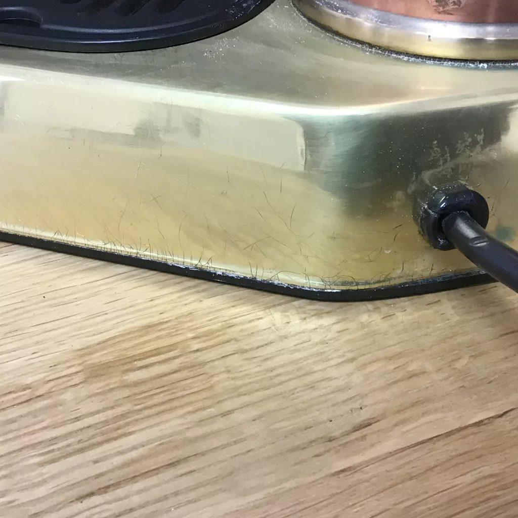 Close-up of a (SOLD) SIDEWALK SALE - PRE-MILLENIUM La Pavoni Professional Copper & Brass Espresso Machine (16 cup USED) with visible scratches and black scuff marks near the edge, on wood surface. Black power cord plugged in. © 2025 1st-line.com