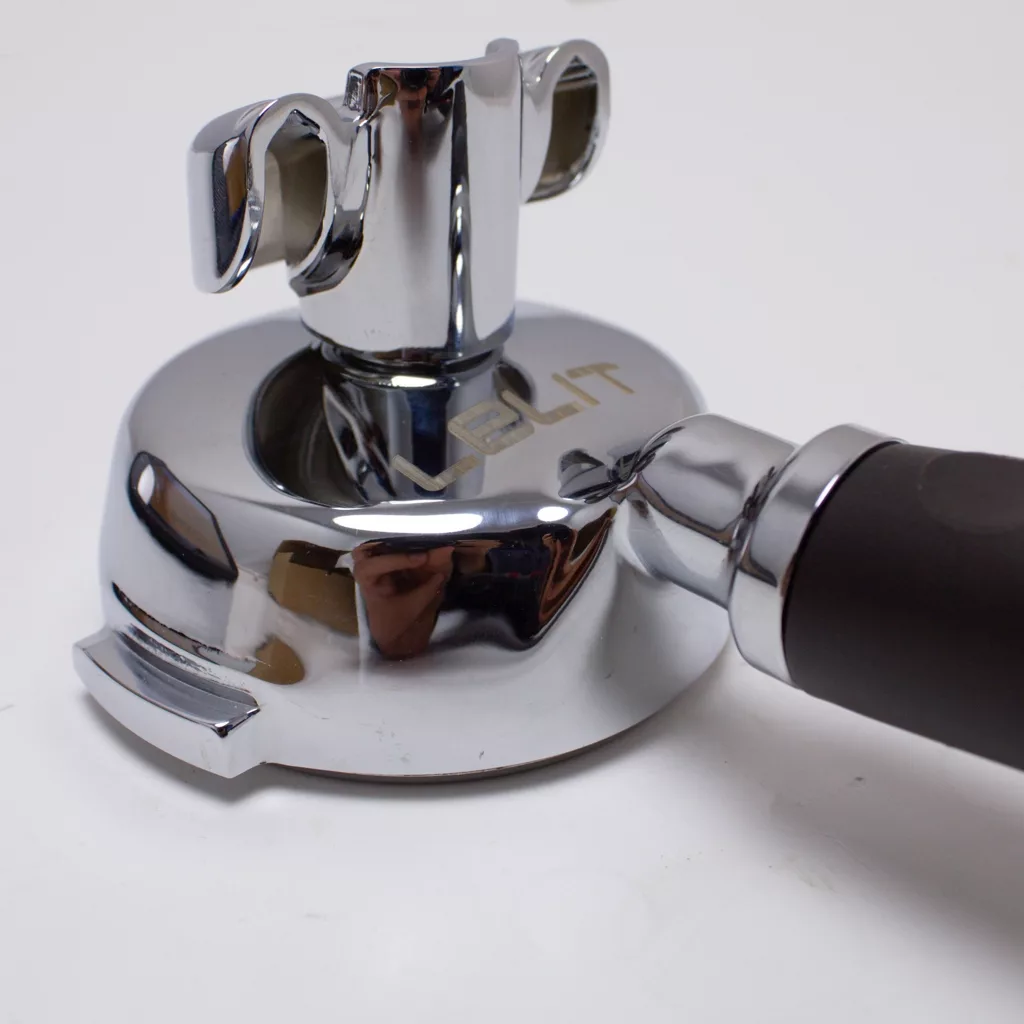 A close-up of a shiny, chrome espresso machine portafilter with a black handle, featuring the brand name LELIT engraved on the top, placed on a white surface. © 2025 1st-line.com