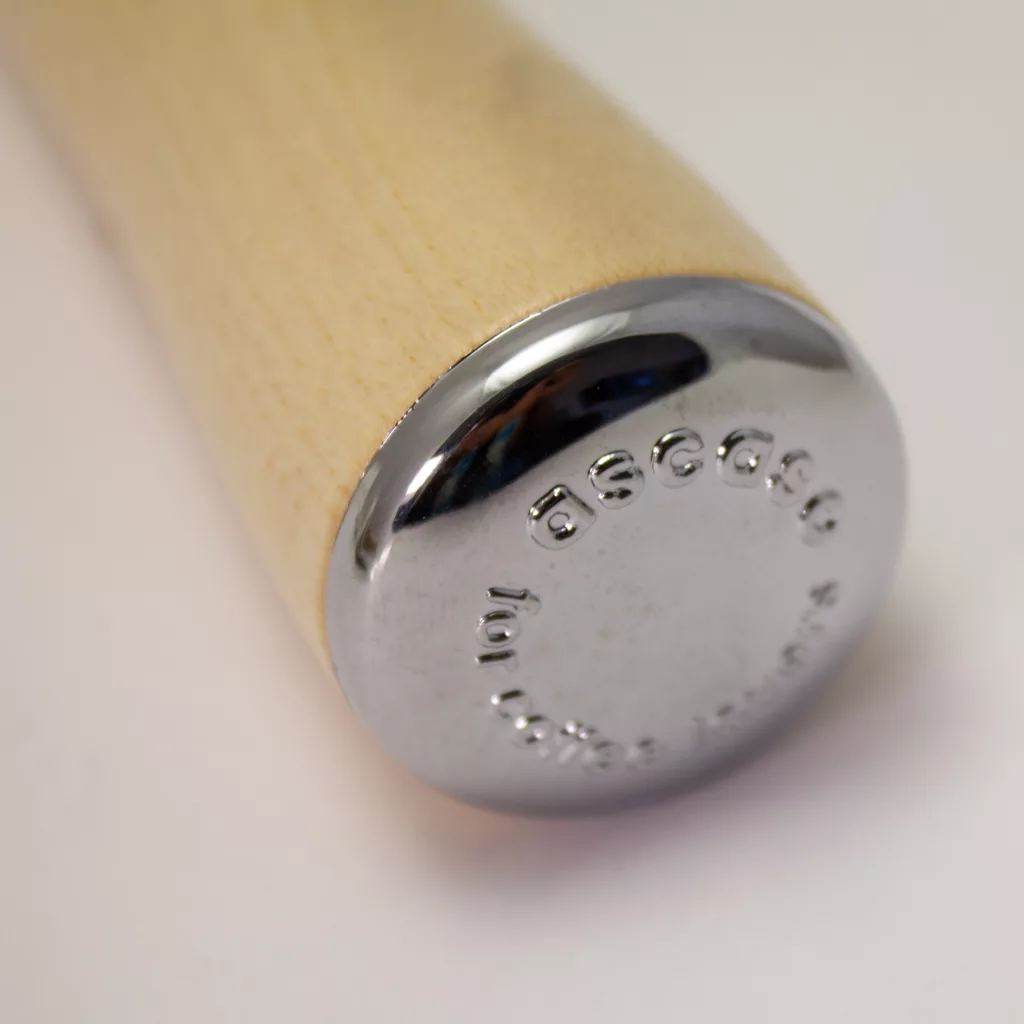 A close-up of the metal end of the DISCONTINUED Ascaso PM259A Wood Portafilter Handle, showing Ascaso and other engraved text on its shiny surface, set against a plain light background. © 2025 1st-line.com